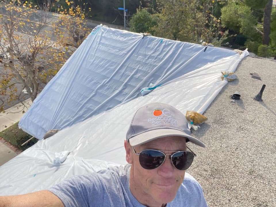 Orange County Restoration team member on a house roof after providing professional roof tarping services.