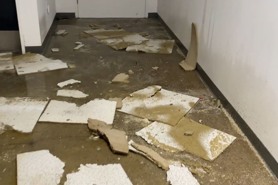 Water-damaged ceiling tiles and debris scattered across a flooded commercial floor